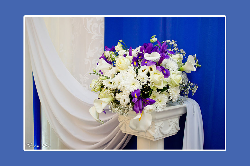 Weiß-violette Blumen auf Säulen neben dem Brautpaartisch
